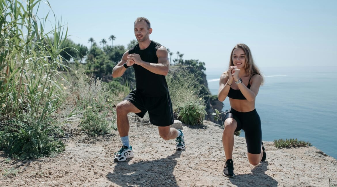 "Homem e mulher a realizar exercício físico ao ar livre, numa paisagem natural com vista para o mar."