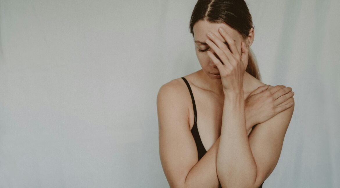 "Mulher com expressão de desconforto e a mão no rosto, sugerindo cansaço ou mal-estar."
