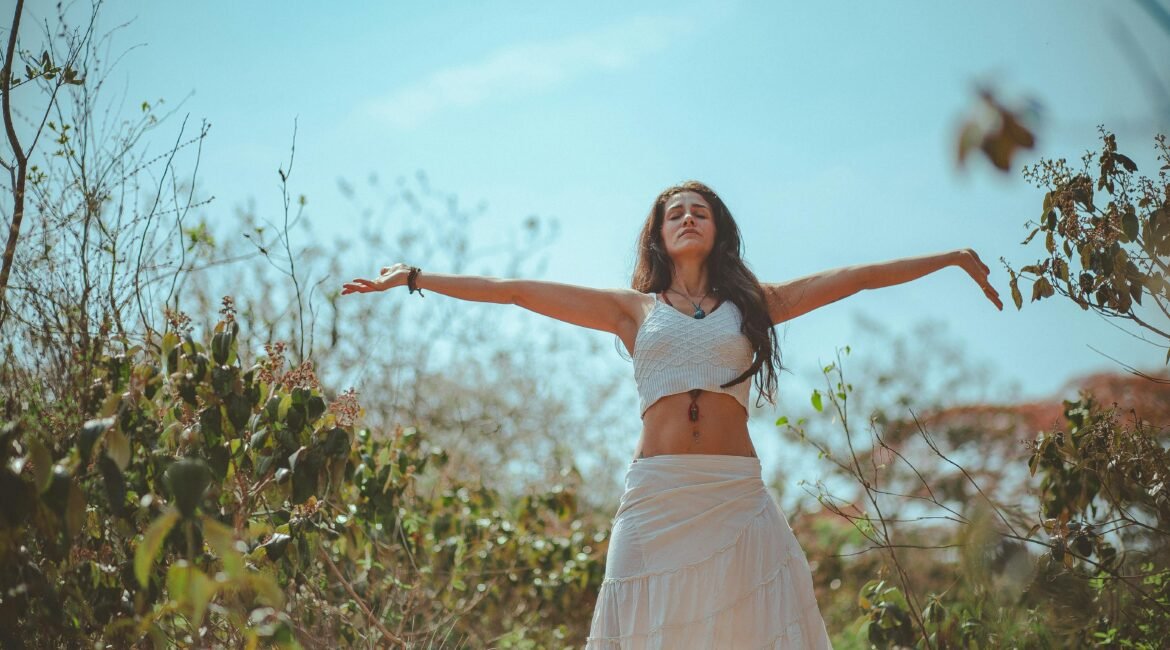 Mulher de braços abertos em meio à natureza, simbolizando equilíbrio, bem-estar e um estilo de vida saudável.