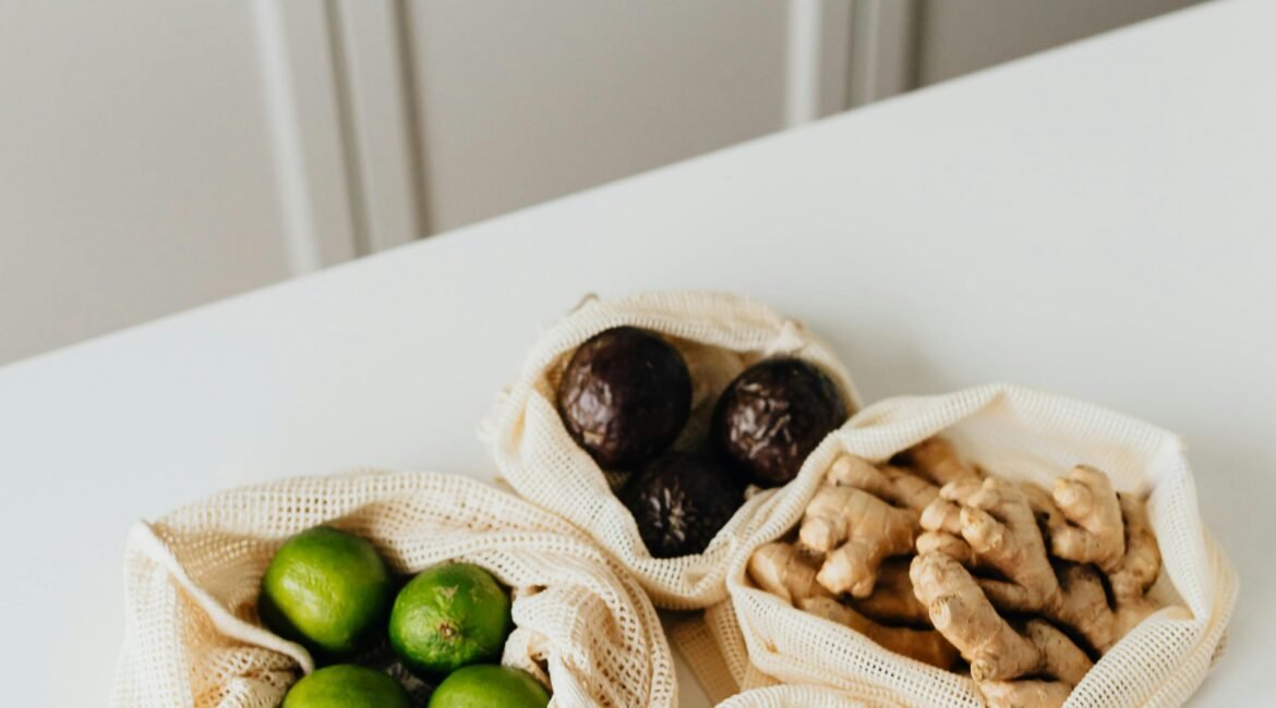 Sacos de pano reutilizáveis com limas, abacates, gengibre e curcuma sobre uma mesa, ilustrando superalimentos quentes e frios na perspetiva da Medicina Tradicional Chinesa.